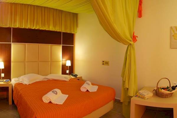 Ein Hotelzimmer im Louros Beach Hotel & Spa mit einem Bett, gelben Vorhängen und einem Korb auf einem Tisch.