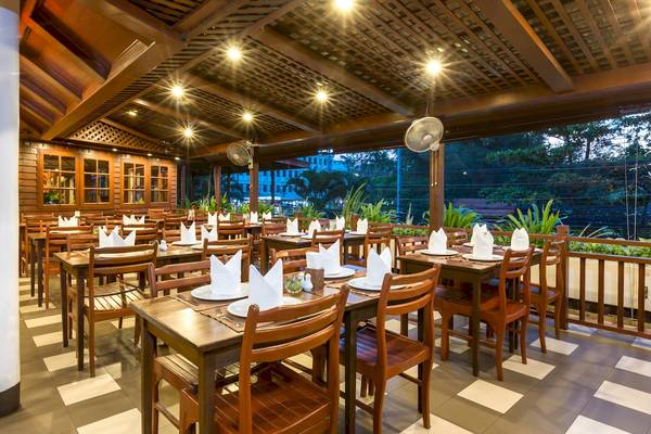 Innenansicht des Restaurants im Best Western Phuket Ocean Resort mit Holztischen und Stühlen, dekorativ gefalteten Servietten und Ausblick auf eine begrünte Außenterrasse.