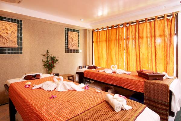 Massageraum im Best Western Phuket Ocean Resort mit zwei Massagebetten, orangefarbenen Decken und Kissen.
