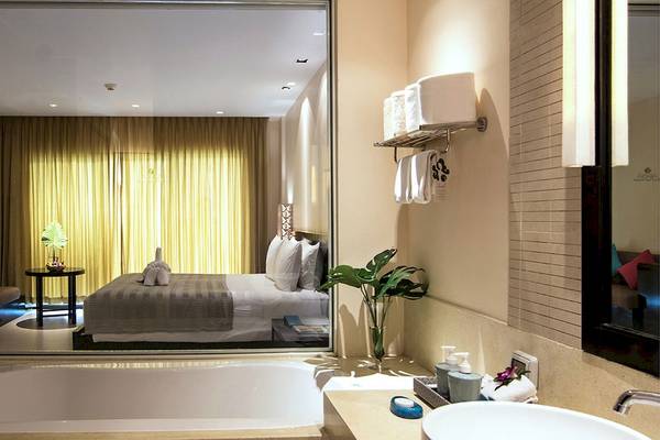 Badezimmer im Apsara Beachfront Resort und Villa mit Badewanne, Spiegel und Bett im Hintergrund.