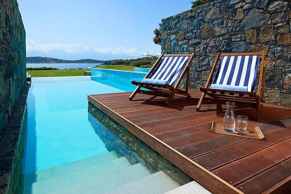 Außenpool des St. Nicolas Bay Resort Hotel mit zwei Liegestühlen und einem Tablett mit Gläsern.