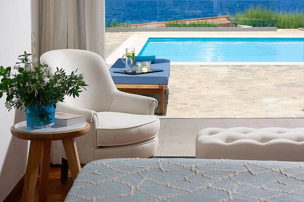 Zimmer mit Poolblick im St. Nicolas Bay Resort Hotel & Villas mit einem weißen Sessel und einem Tisch.