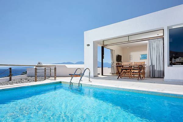 Außenpool des St. Nicolas Bay Resort Hotel mit Blick auf das Meer und eine Terrasse mit Tisch und Stühlen.