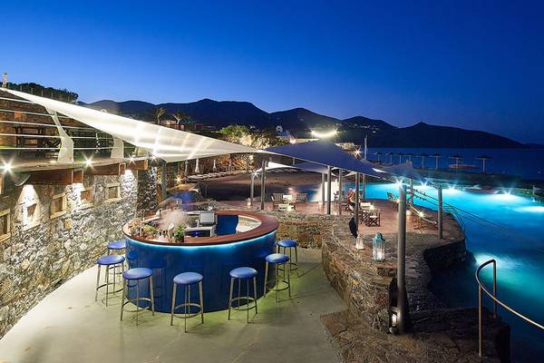 Abendansicht der Poolbar im St. Nicolas Bay Resort Hotel & Villas mit blau beleuchteten Stühlen und Blick auf den Pool und die Berge