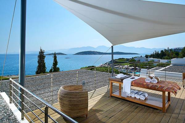 Außenterrasse des St. Nicolas Bay Resort Hotel & Villas mit Blick auf das Meer, Liegestuhl, Handtücher und ein Sonnenschirm.
