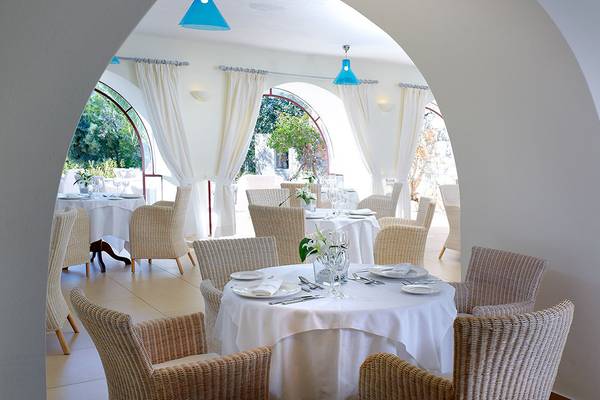 Innenansicht des Restaurants im St. Nicolas Bay Resort Hotel & Villas mit runden Bögen, weißen Tischdecken und blauen Lampen.