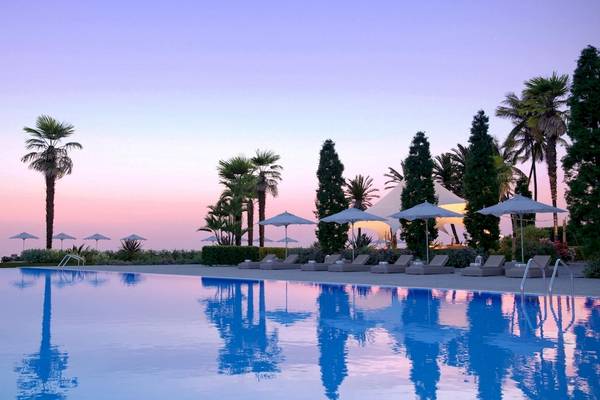 Pool mit Sonnenliegen und Palmen am Ikos Andalusia Hotel bei Sonnenuntergang