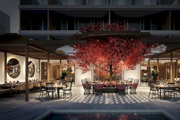 Innenbereich des Ikos Andalusia Hotels mit zentralem rot blühendem Baum, Tischen und Stühlen um das Atrium.