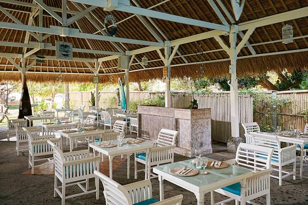 Außenbereich des Sol Benoa Bali Restaurants mit weißen Tischen und Stühlen unter einem Strohdach.