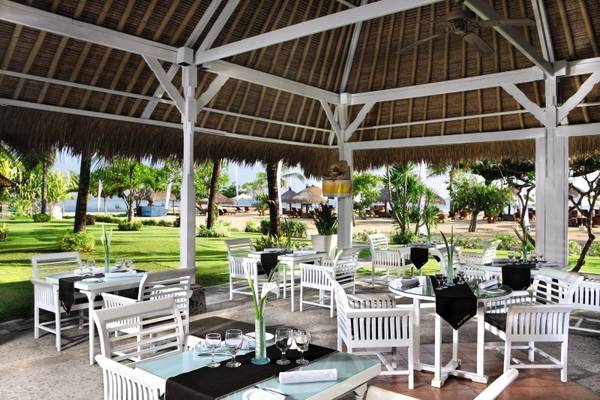 Außenbereich des Sol Benoa Bali Restaurants mit weißen Tischen und Stühlen unter einem Strohdach.