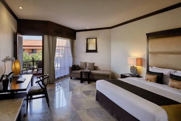 Innenansicht eines Zimmers im Sol Benoa Bali Hotel mit großem Bett, Fernseher und Balkon.