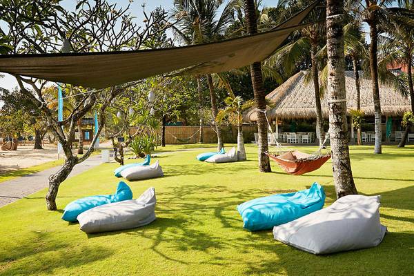 Gartenbereich des Sol Benoa Bali Hotels mit mehreren Sofas und einem Sonnenschirm.