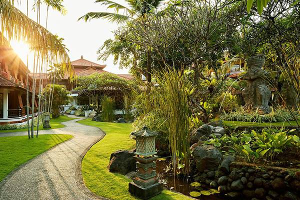 Gartenansicht des Sol Benoa Bali Hotels mit gepflastertem Weg und Wassergarten.