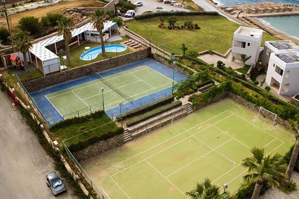 Luftaufnahme des Tennisplatzes im Royal Blue Resort mit einem Pool und Häusern im Hintergrund.