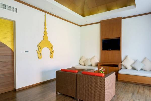Wohnbereich des Beyond Resort Khao Lak mit modernen Möbeln, Fernseher und gelber Wanddekoration.