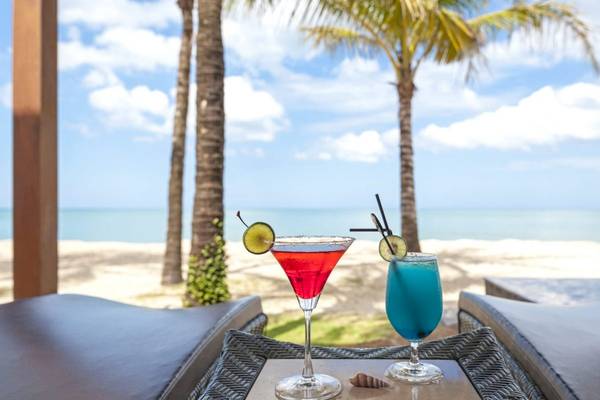 Zwei Cocktails auf einem Tisch mit Blick auf den Ozean und Palmen im Hintergrund.