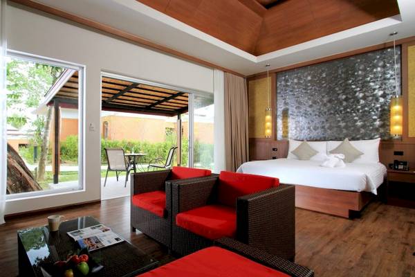 Innenansicht eines Zimmers im Beyond Resort Khao Lak mit einem großen Bett, roten Stühlen und einem Tisch vor einer Glaswand.
