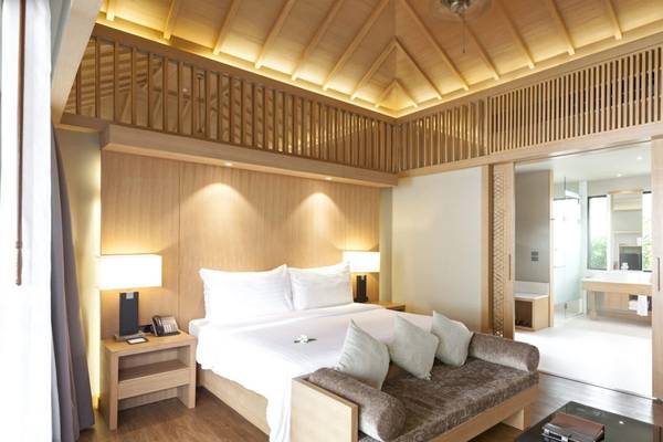 Ein modernes Hotelzimmer im Beyond Resort Khao Lak mit Holzelementen, einem großen Bett und einem offenen Badezimmerbereich.