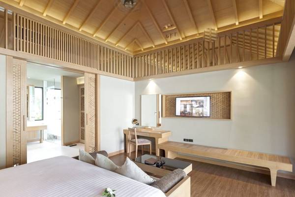 Innenansicht eines Zimmers im Beyond Resort Khao Lak mit einem großen Bett, Holzmöbeln und einem Fernseher an der Wand.