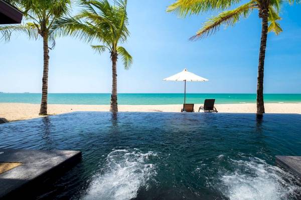 Strand des Beyond Resort Khao Lak mit zwei Strandstühlen und einem Schirm sowie einem Pool