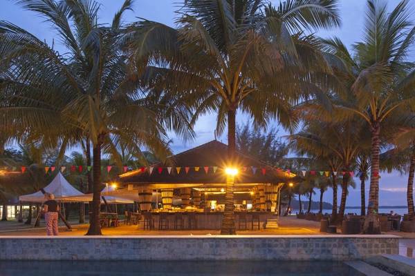 Nachtansicht der Poolbar des Beyond Resorts Khao Lak mit Palmen und einer Person, die einen Koffer trägt.