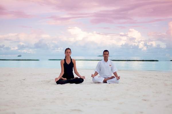 Ein Paar praktiziert Yoga auf dem Strand des Constance Halaveli Maldives.
