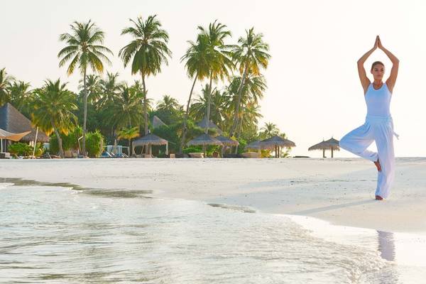 Frau beim Yoga auf einem Strand im Constance Halaveli Maldives