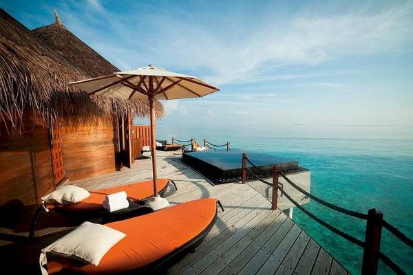 Terrasse des Constance Halaveli Maldives mit Sonnenliegen, einem Schirm und Blick auf das Meer.
