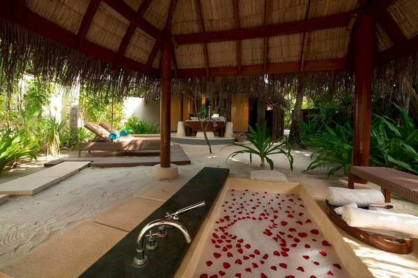 Außenbereich des Constance Halaveli Maldives mit einer Badewanne unter einem Hut und roten Rosenblättern.