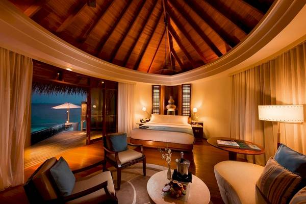 Innenansicht der Suite im Constance Halaveli Maldives mit Bett, Wohnzimmer, Tisch und Blick auf das Meer.