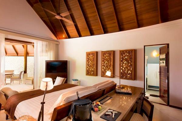 Innenansicht eines Schlafzimmers im Constance Halaveli Maldives Hotel mit Doppelbett, Tisch, Fernseher und offenen Türen.