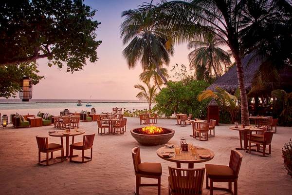 Außenbereich des Constance Halaveli Maldives mit Garten, Feuerstelle und Blick auf den Sonnenuntergang.
