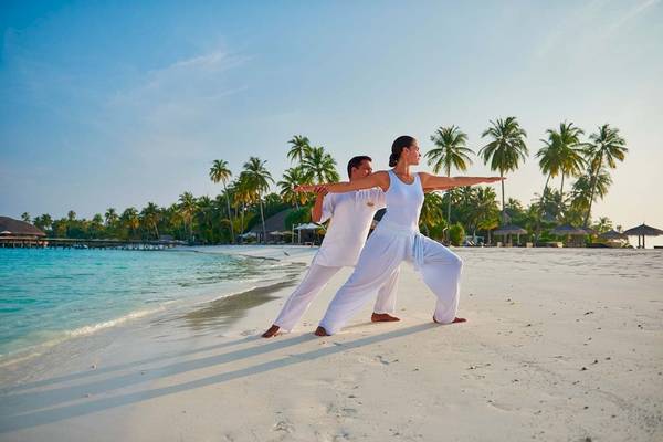 Ein Paar praktiziert Yoga am Strand des Constance Halaveli Maldives Hotels.