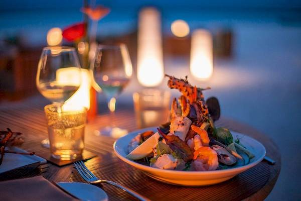 Essen bei Kerzenschein im Constance Halaveli Maldives mit Gericht, Weinglas und Dekoration.