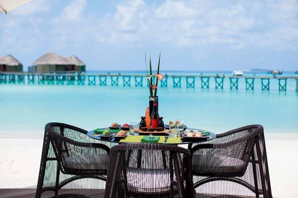 Tisch am Strand im Constance Halaveli Maldives mit Blick auf eine Brücke und das Meer.