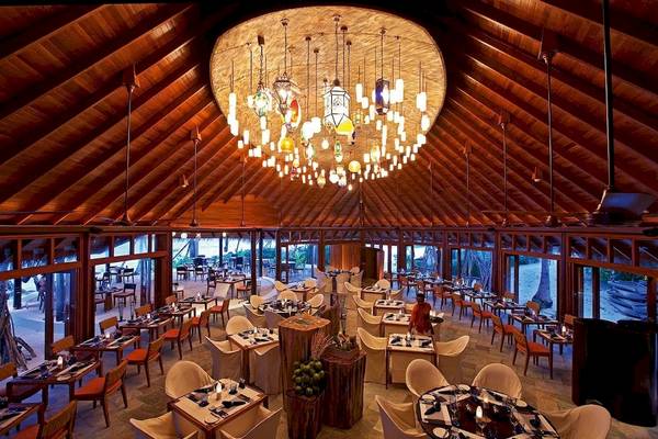 Innenbereich des Restaurants im Constance Halaveli Maldives mit vielen Tischen und Stühlen, einer großen Kronleuchter und einer Person im Hintergrund.