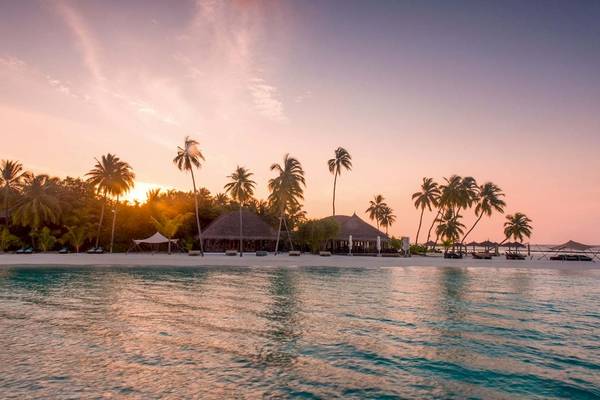 Sonnenuntergang am Strand des Constance Halaveli Maldives mit Palmen und Gebäuden.