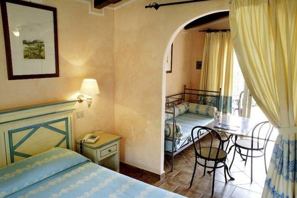 Ein Zimmer im Colonna Country & Sporting Club mit einem Doppelbett, Nachttisch, Lampe und einem kleinen Esstisch.
