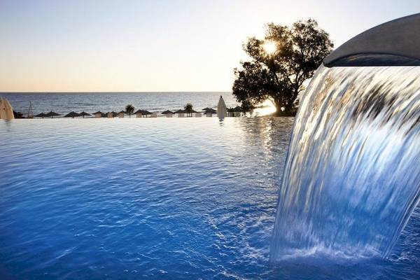 Wasserfall im Außenpool des Atlantica Eleon Grand Resorts mit Blick auf das Meer und Sonnenuntergang