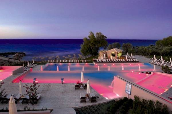 Abendlicher Blick auf den Poolbereich des Atlantica Eleon Grand Resorts mit pink beleuchtetem Wasser.