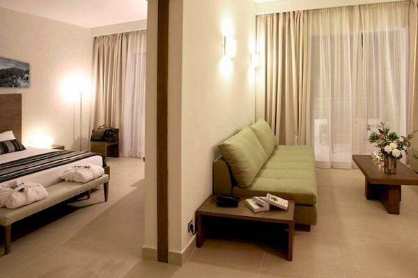 Innenansicht eines Zimmers im Atlantica Eleon Grand Resort mit Bett, Sofa und Tisch.