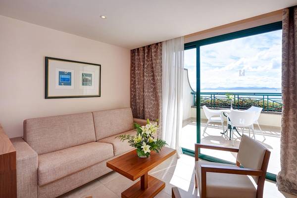 Balkonbereich im Hipotels Natura Palace Hotel mit Sofa, Tisch, Blumen und Meerblick.