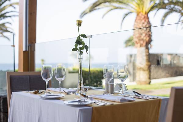 Ein Tisch im Restaurant mit Aussicht auf den Ozean, gedeckt mit einem gelben Tischtuch, Gläsern und Besteck.