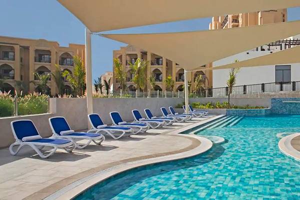 Pool im DoubleTree by Hilton Resort & Spa Marjan Island mit Sonnenliegen und Gebäuden im Hintergrund.