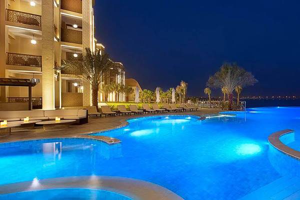 Außenpool des DoubleTree by Hilton Resort & Spa Marjan Island bei Nacht mit Lounge-Bereich und Palmen.