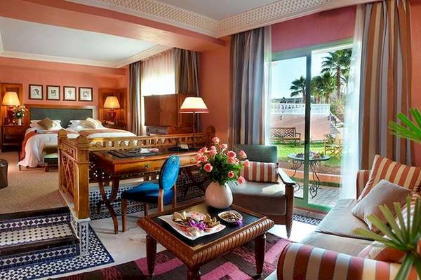 Innenansicht eines Zimmers im Palmeraie Palace Hotel mit Bett, Schreibtisch, Sofa und Gartenblick.