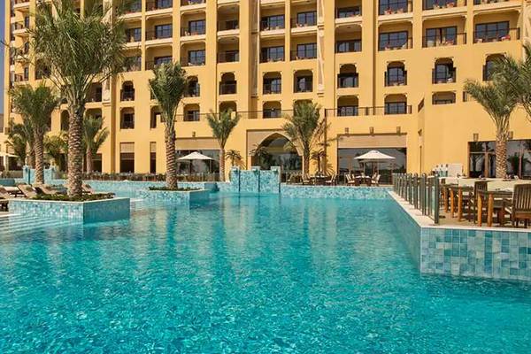 Außenpool des DoubleTree by Hilton Resort & Spa Marjan Island mit Loungeliegen und einem Gebäude im Hintergrund.