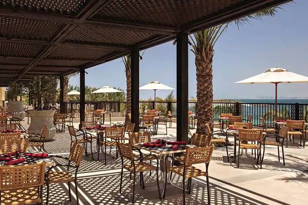 Terrasse des DoubleTree by Hilton Resort & Spa Marjan Island mit Tischen und Stühlen unter Schirmen.
