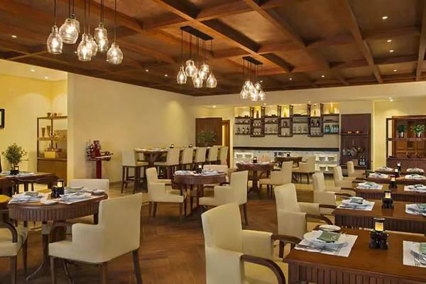 Innenbereich eines Restaurants im DoubleTree by Hilton Resort & Spa Marjan Island mit Holztischen, Stühlen und Kronleuchtern.
