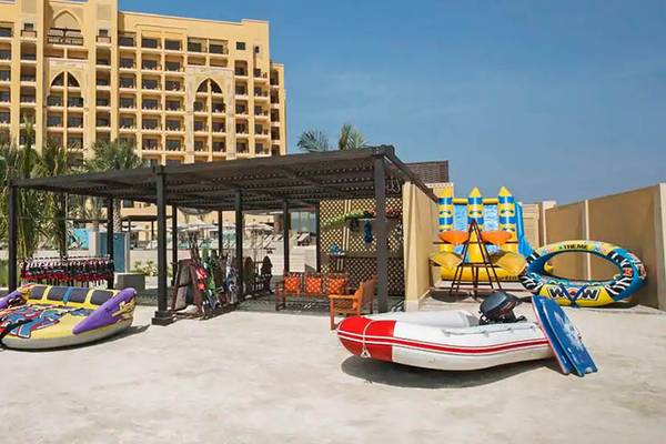 Strand mit Lounge-Stühlen und Wassersportgeräten vor dem DoubleTree by Hilton Resort & Spa Marjan Island